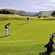 Un jugador de golf alinea su pelota mientras otro jugador sostiene la bandera